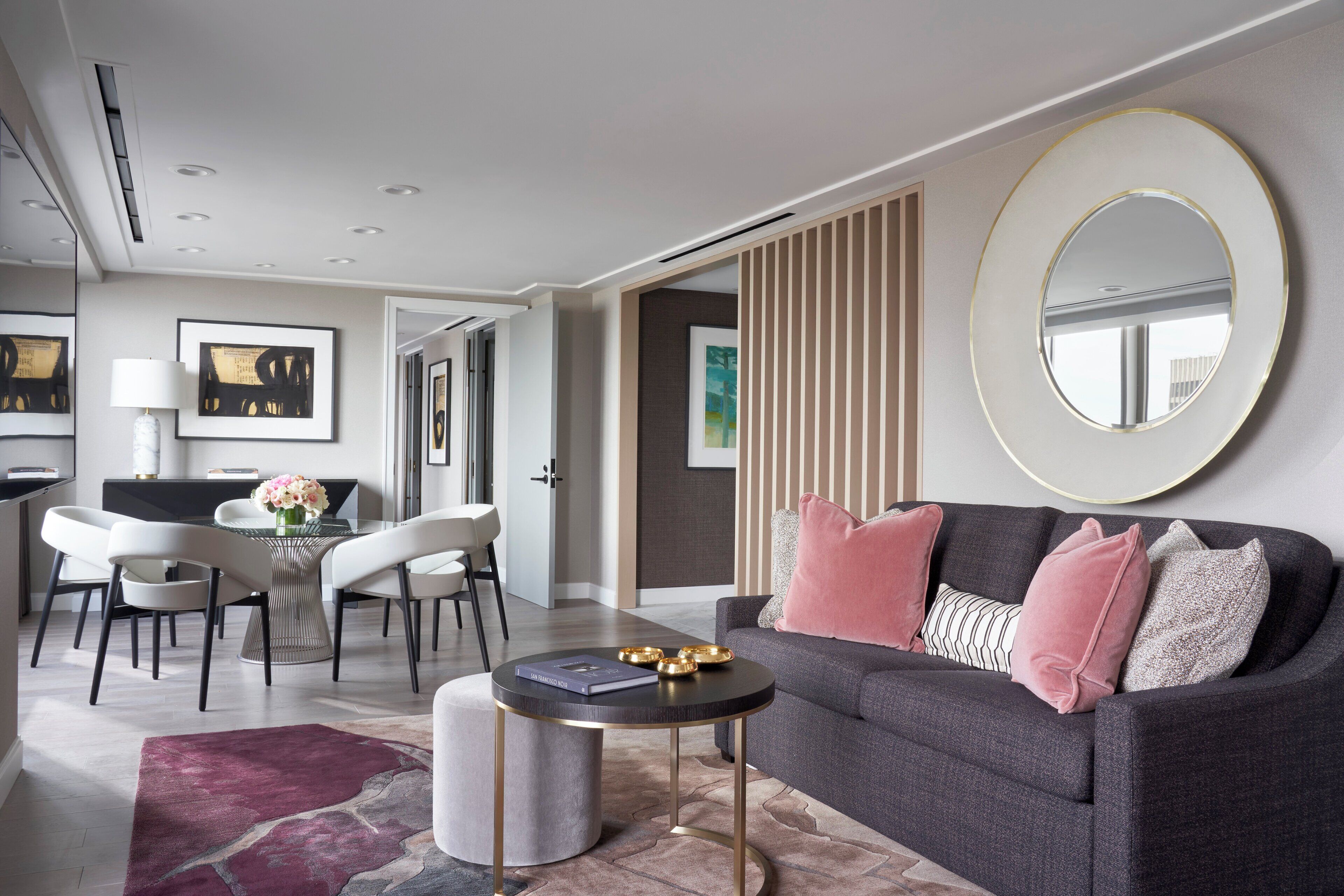 A modern living room with a grey sofa, round coffee table, and a dining area with a white table and chairs.