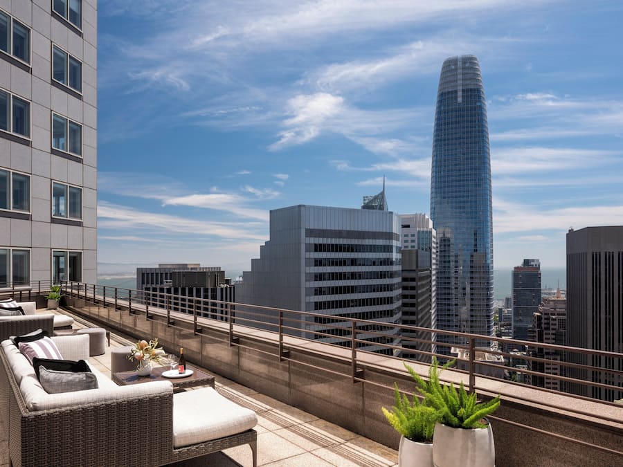 A rooftop terrace with outdoor seating, a view of the city skyline, and a modern building in the background.