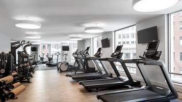 A modern gym with multiple treadmills, weight machines, and a large window offering a city view.