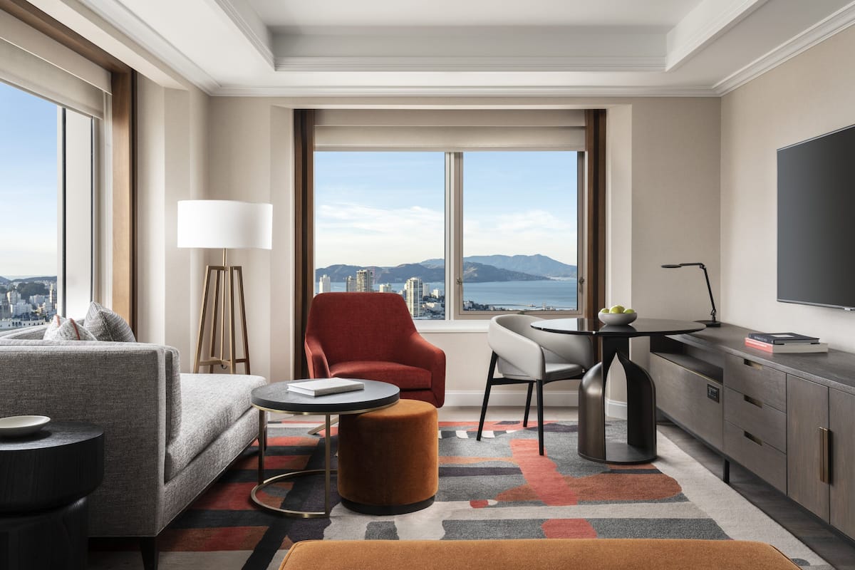 Una habitación de hotel moderna con sofá, sillón, mesa de comedor y televisor.