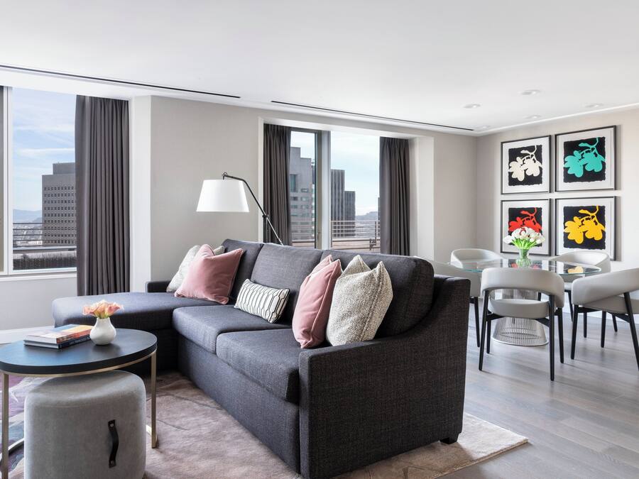 A modern living room with a grey sectional sofa, a round coffee table, a side table, and a dining area with chairs.