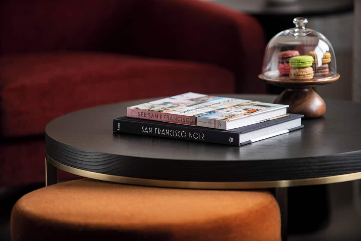 Una mesa redonda con dos libros titulados 'See San Francisco' y 'San Francisco Noir', y una cúpula de vidrio con macarons.