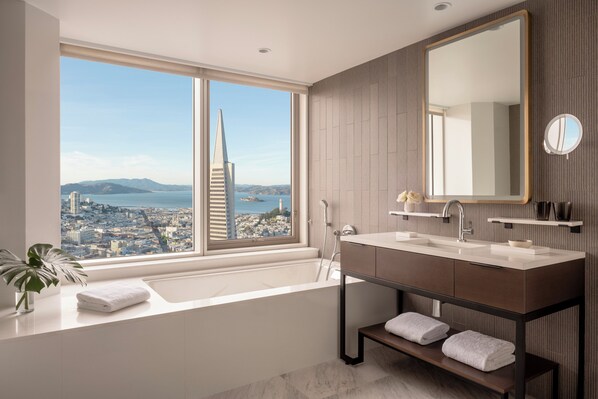 A modern bathroom with a large window, a bathtub, a vanity with a mirror, and a view of a cityscape and a tall building. - Four Seasons Hotel San Francisco at Embarcadero (San Francisco)