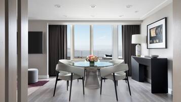 A modern dining area with a round table, white chairs, and a vase of flowers. There is a large window with a view of the cityscape.