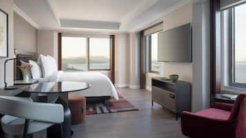 Une chambre d’hôtel moderne dotée d’un grand lit, d’un bureau avec une chaise, d’une télévision et offrant une vue sur la ville et les montagnes.