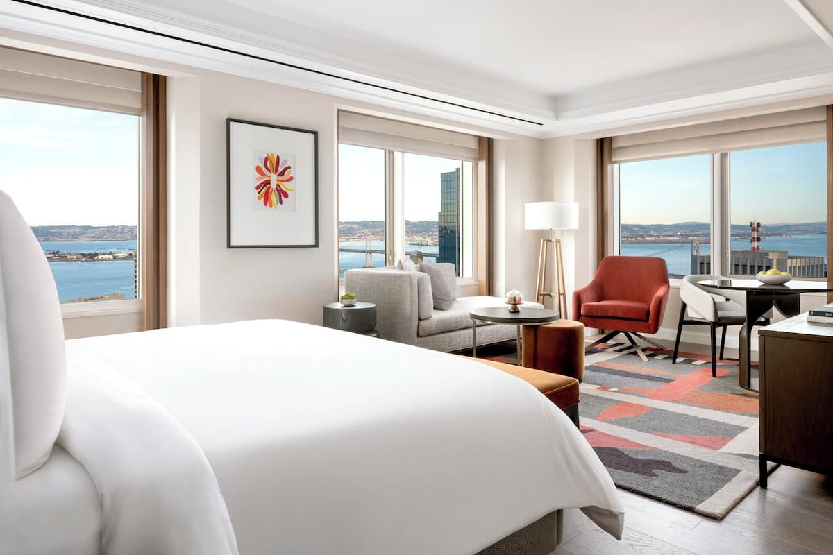 Habitación de hotel con una cama grande, un sofá, una silla, un escritorio y vistas a la ciudad y al agua.
