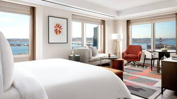 A hotel room with a large bed, a sofa, a chair, a desk, and a view of the city and water.
