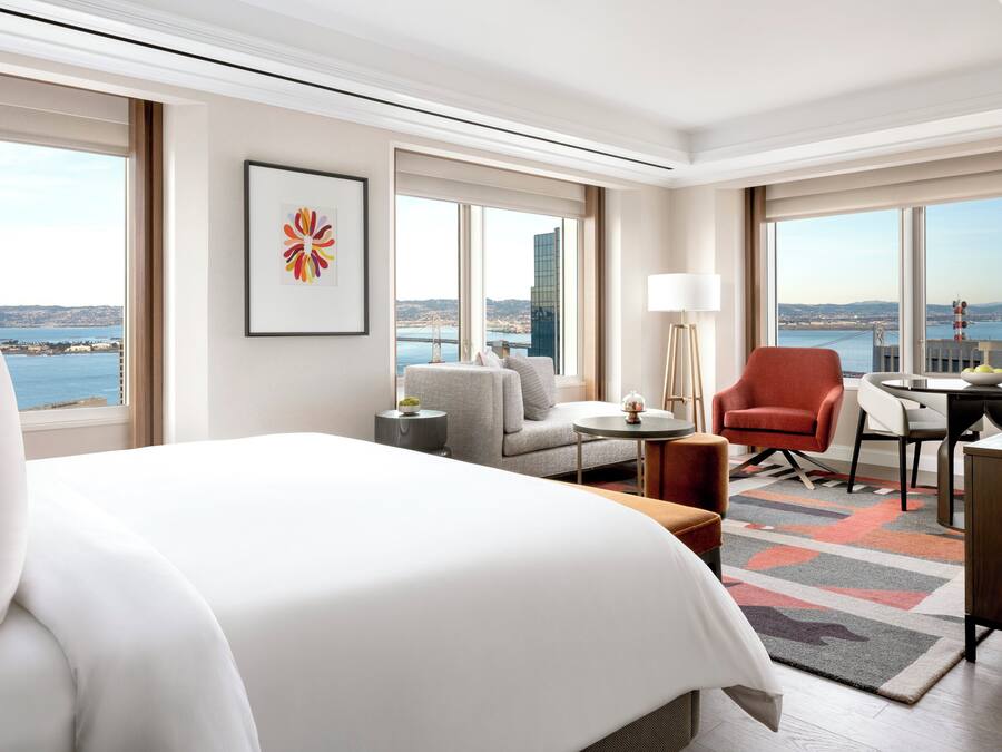A hotel room with a large bed, a sofa, a chair, a desk, and a view of the city and water.