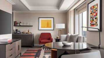 Een moderne hotelkamer met een zithoek, een rode fauteuil, een bank, een stadsgezicht schilderij en een lamp.