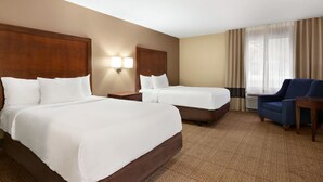 A hotel room with two beds, a desk, a chair, and a large window with curtains.