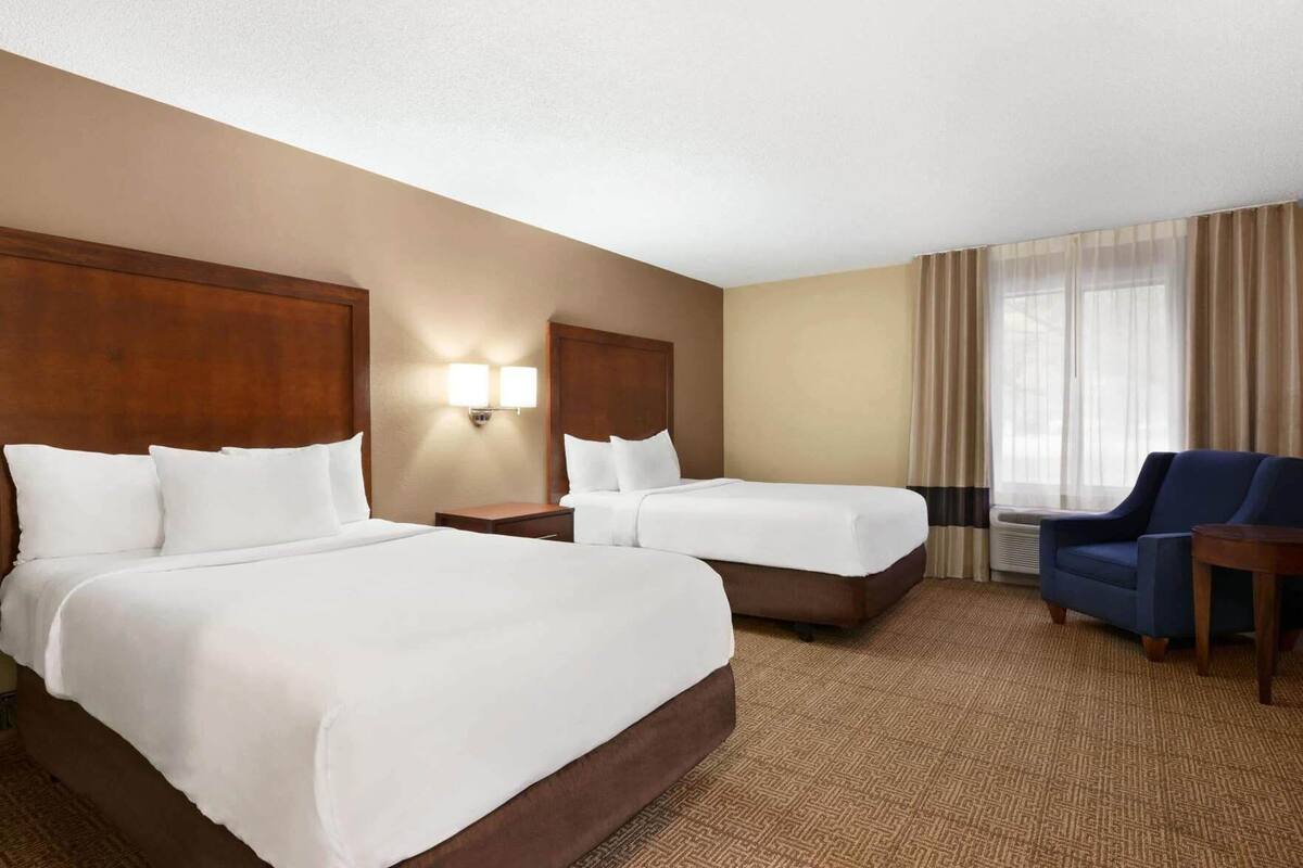 A hotel room with two beds, a desk, a chair, and a window with curtains.