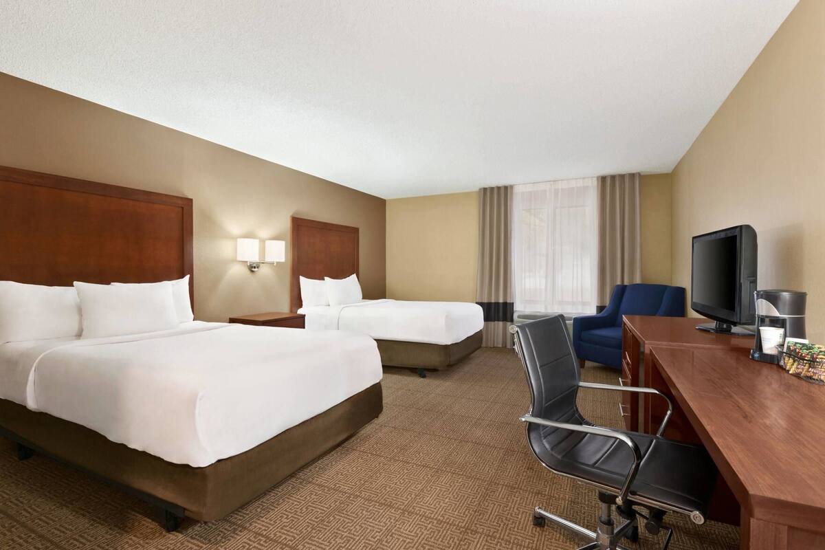 A hotel room with two beds, a desk, a chair, a television, and a coffee maker.
