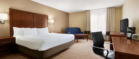 Habitación de hotel con una cama grande, un escritorio con silla, televisión y ventana con cortinas.