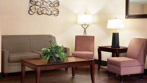A living room with a brown sofa, a matching armchair, a coffee table with a plant, two wall-mounted lamps, and a decorative wall piece.
