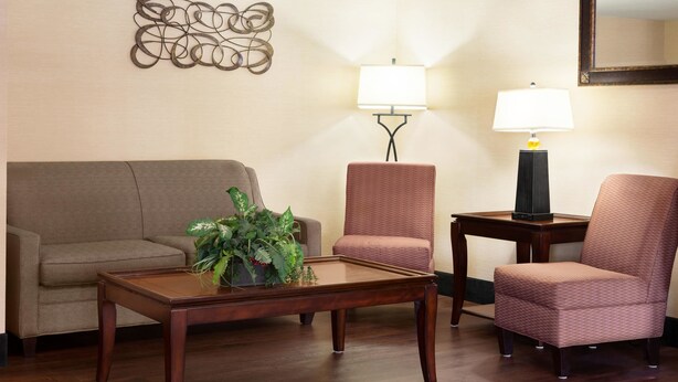 A living room with a brown sofa, a matching armchair, a coffee table with a plant, two wall-mounted lamps, and a decorative wall piece. - Baymont by Wyndham Rocky Mount (Rocky Mount)
