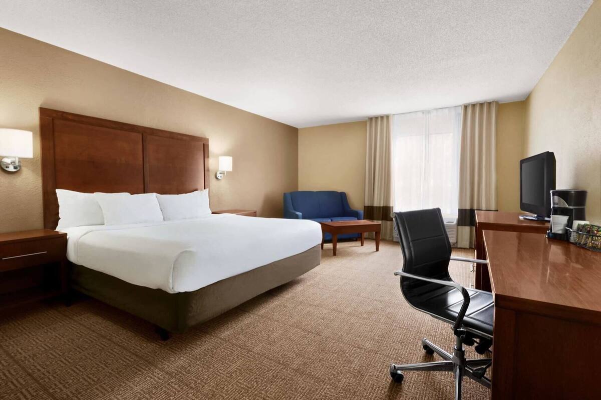 A hotel room with a large bed, a desk with a computer, a chair, a TV, and a window with curtains.