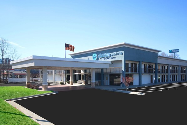 A modern hotel building with a covered entrance, a parking lot, and an American flag.