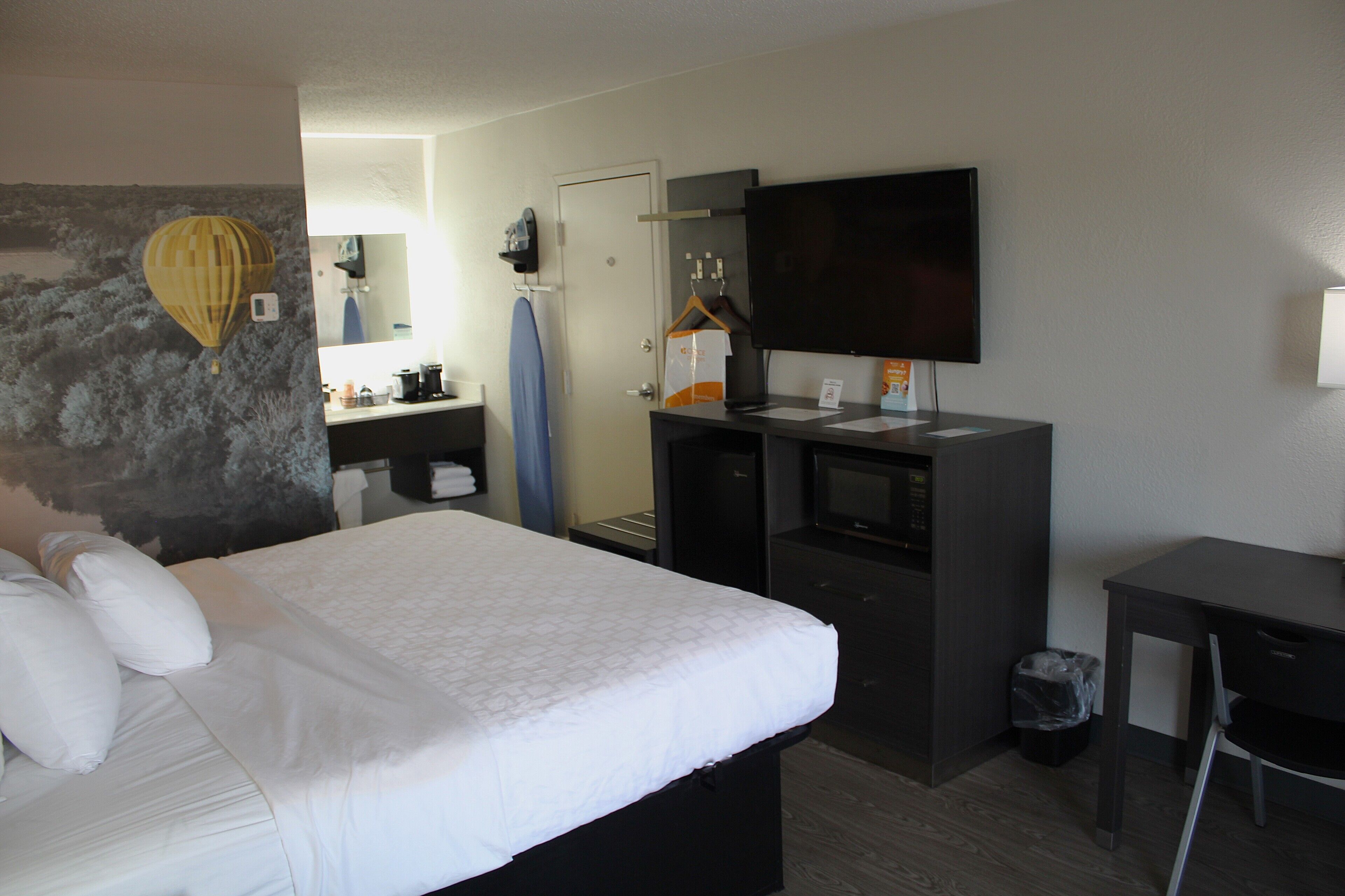 A hotel room with a bed, a desk, a TV, a mirror, and a bathroom visible through an open door.