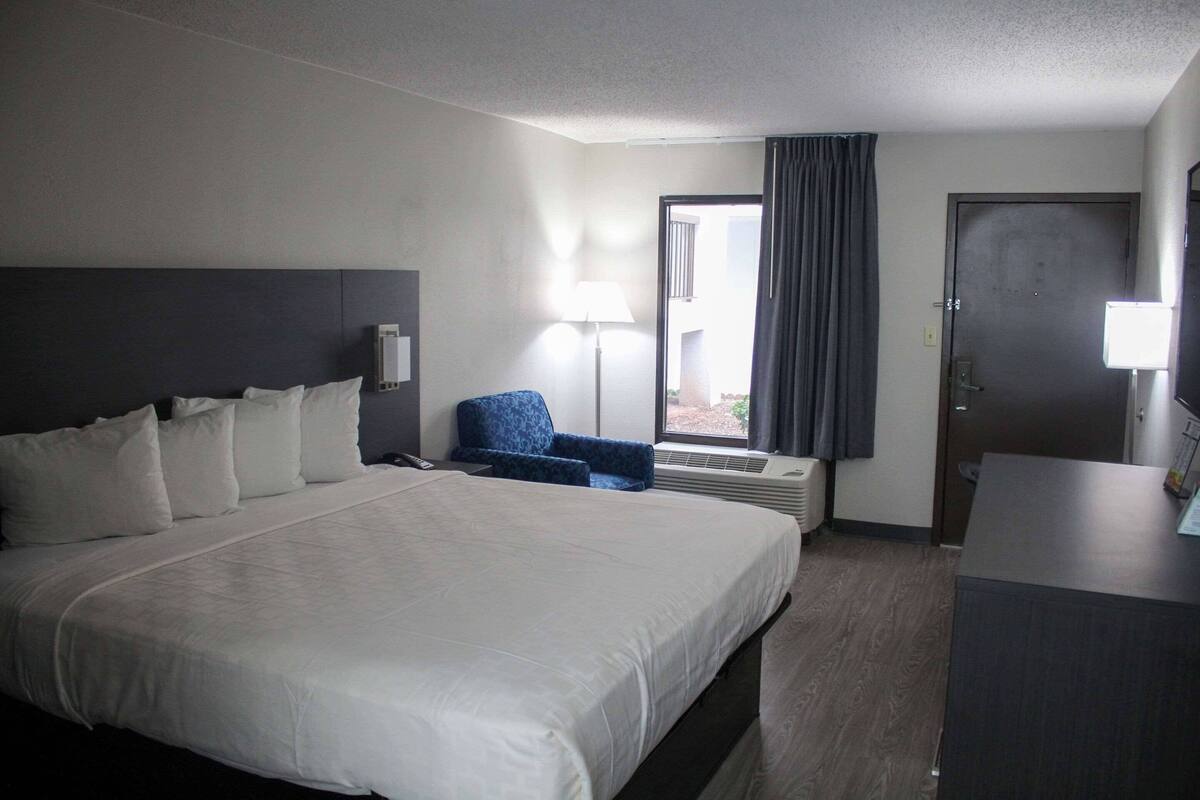 Ein Hotelzimmer mit einem großen Bett, einem Schreibtisch, einem Stuhl, einer Lampe und einer Tür.