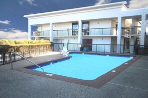 A swimming pool with a metal ladder, surrounded by a fence, and a building with multiple balconies in the background.