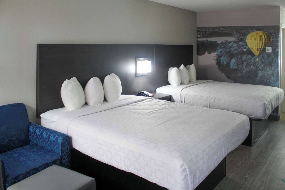 Ein Hotelzimmer mit zwei Betten, einem Nachttisch, einem Sessel und einem Wandgemälde.