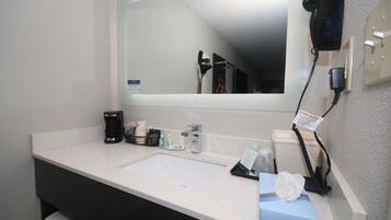 A hotel bathroom with a white sink, a mirror, a hairdryer, and toiletries.