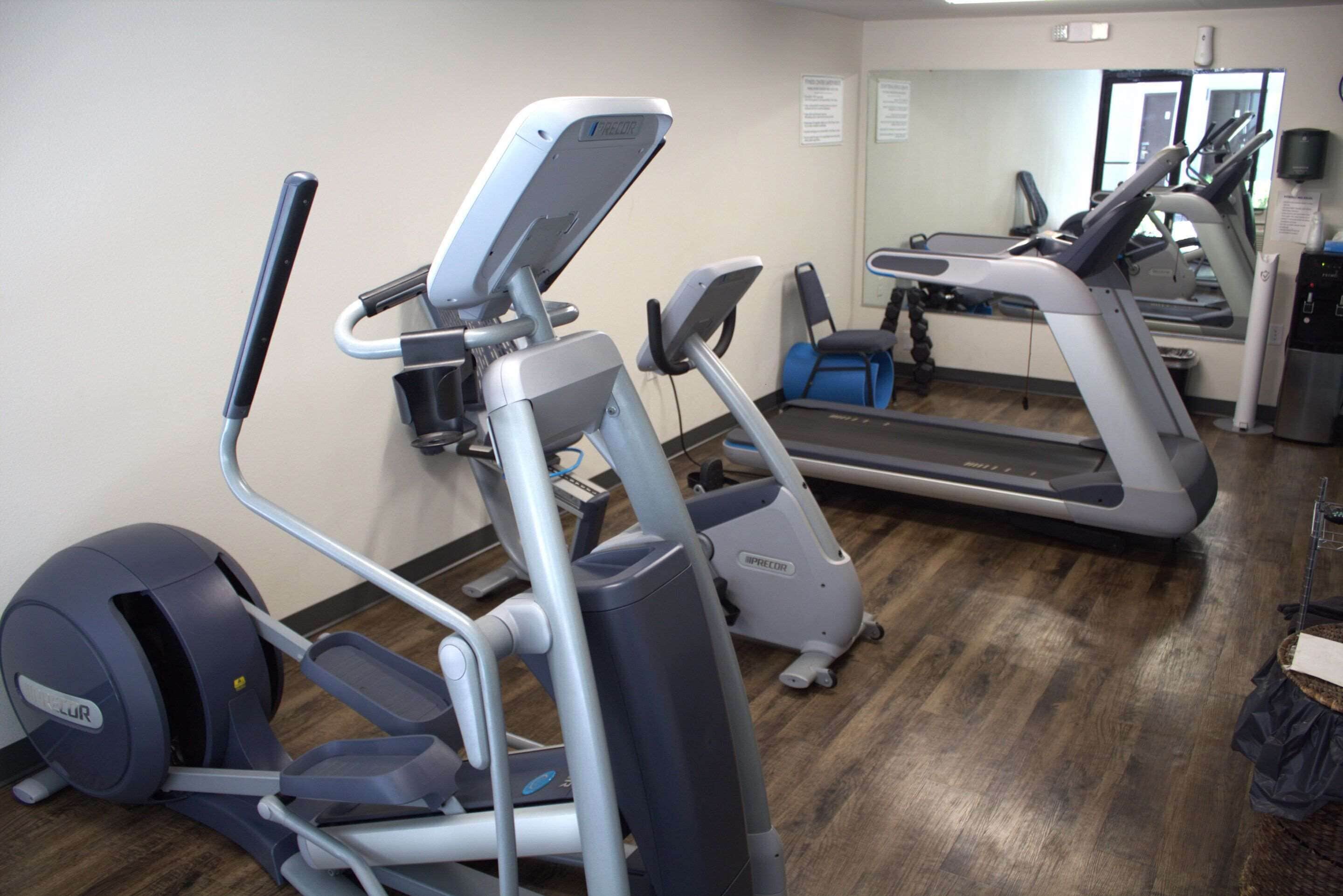 A gym with treadmills, ellipticals, and a mirrored wall.