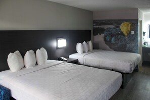 A hotel room with two beds, a nightstand, a wall-mounted lamp, and a mural of a hot air balloon.