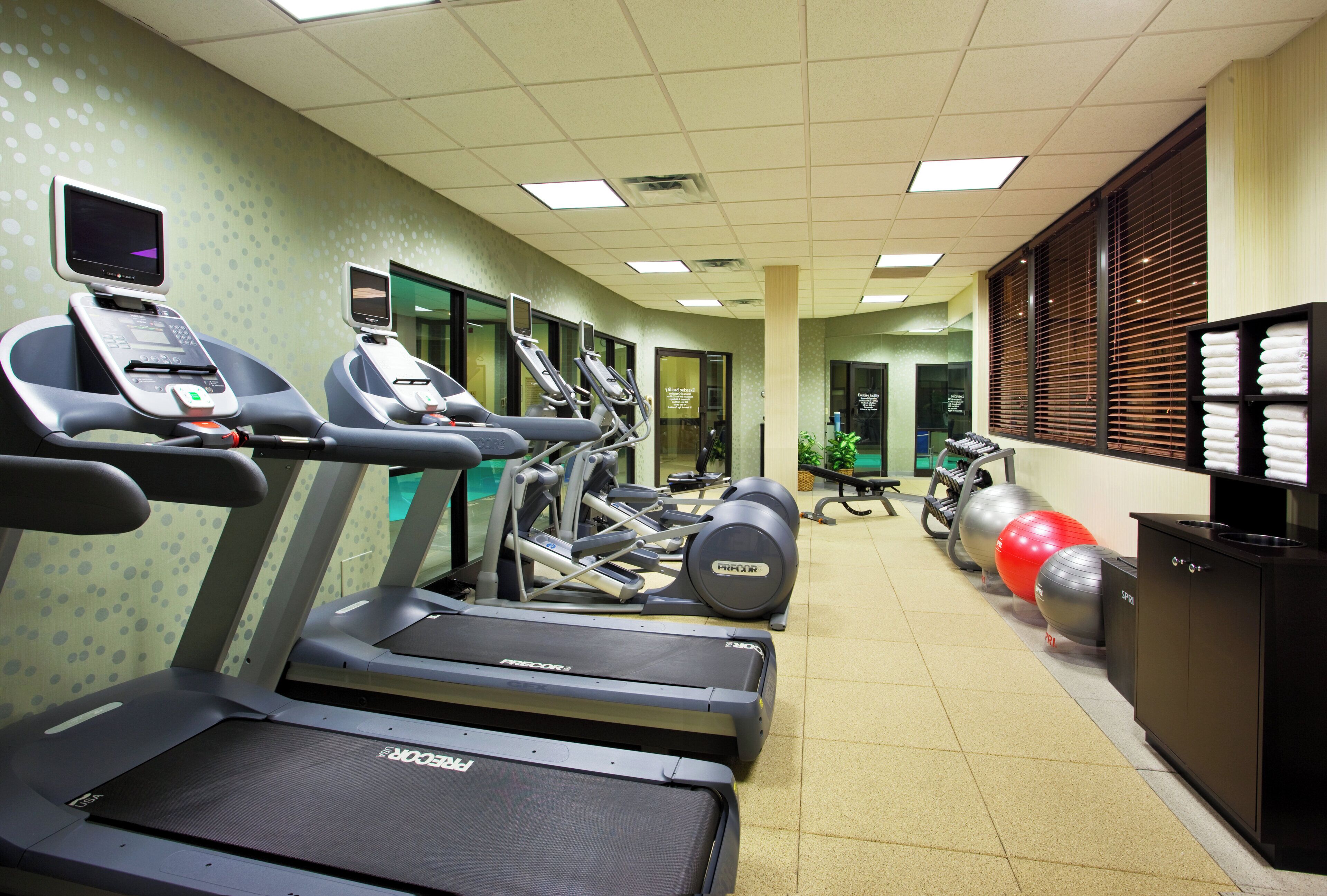 Une salle de sport équipée de tapis de course, de ballons d’exercice et d’un écran fixé au mur.