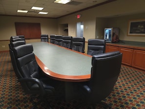 A conference room with a long table and multiple chairs, a patterned carpet, and a cabinet with a television.