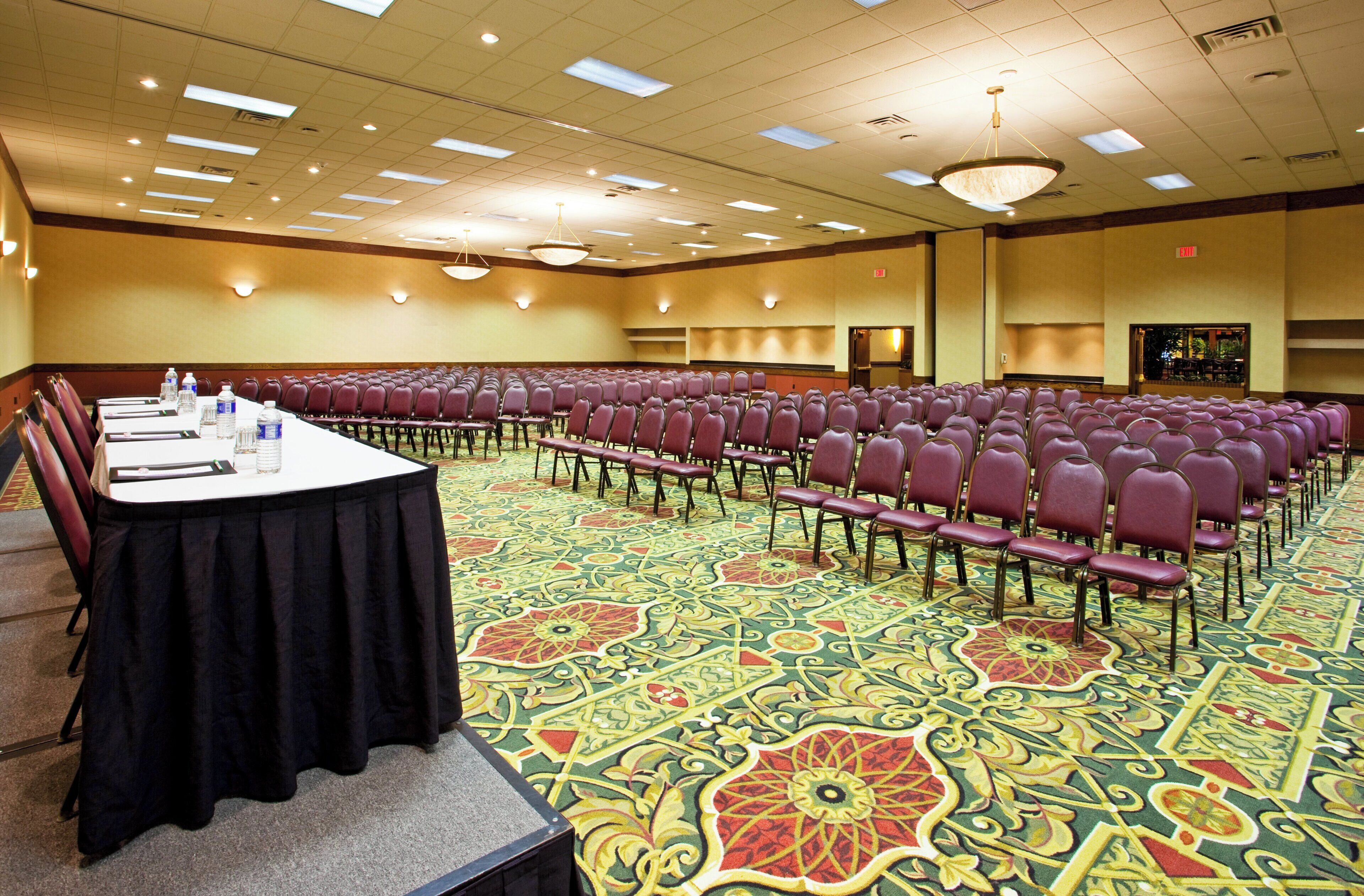 A conference room with rows of chairs, a long table with water bottles, and a patterned carpet.