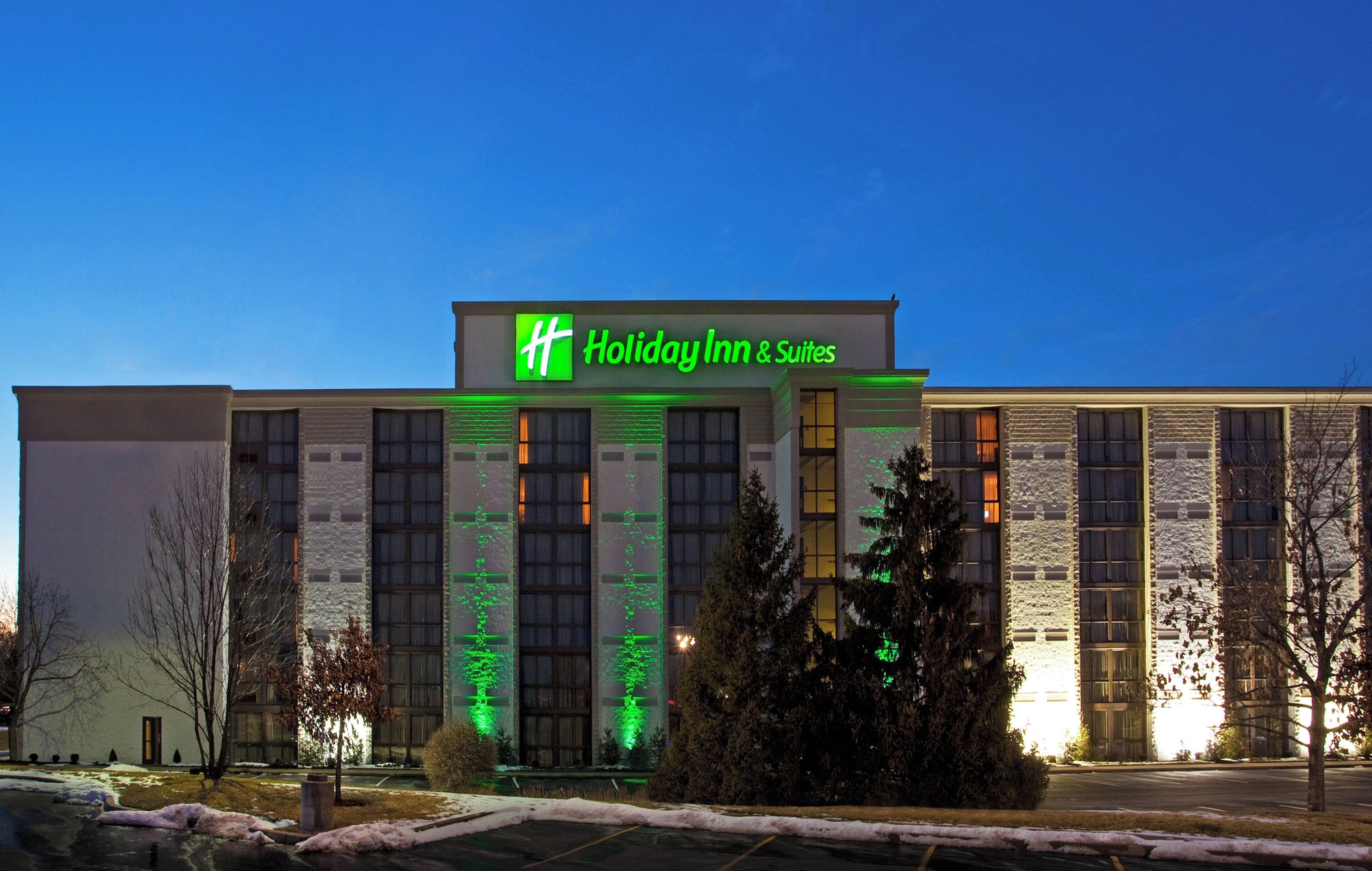 Edificio de Holiday Inn & Suites con un letrero verde llamativo, ventanas grandes y un estacionamiento con nieve.