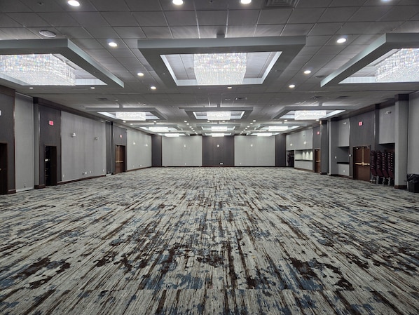 A large, empty conference room with a patterned carpet, recessed lighting, and skylights.