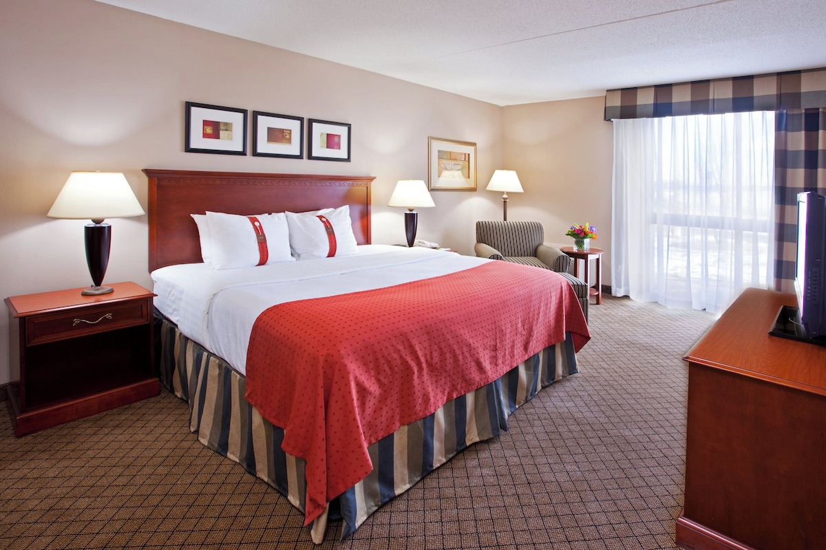 A hotel room with a large bed, two bedside tables with lamps, a desk, and a chair.