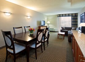 Habitación de hotel con una mesa de comedor, sillas, un sofá, un televisor, una lámpara y un microondas.