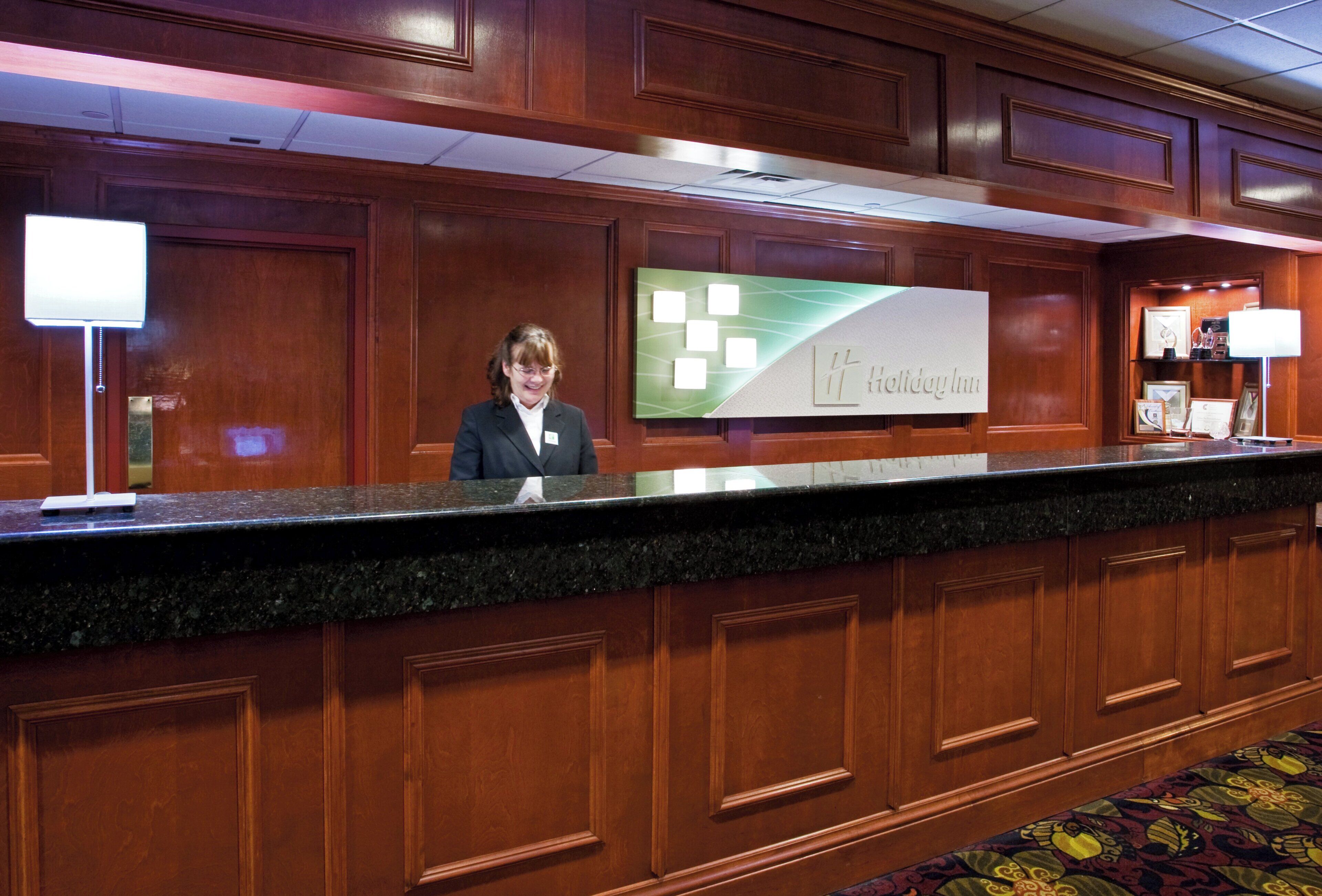 A reception desk with a sign for Holiday Inn, wooden paneling, and a carpeted floor.