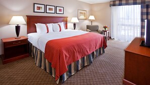 Quarto de hotel com uma cama grande, duas mesas de cabeceira com luminárias, uma escrivaninha com cadeira e uma janela com cortinas.