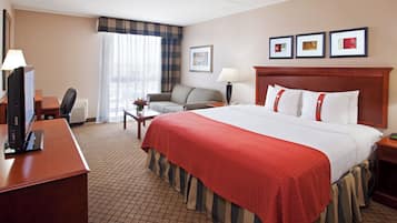 A hotel room with a large bed, a desk with a computer, a chair, a lamp, and a window with curtains.