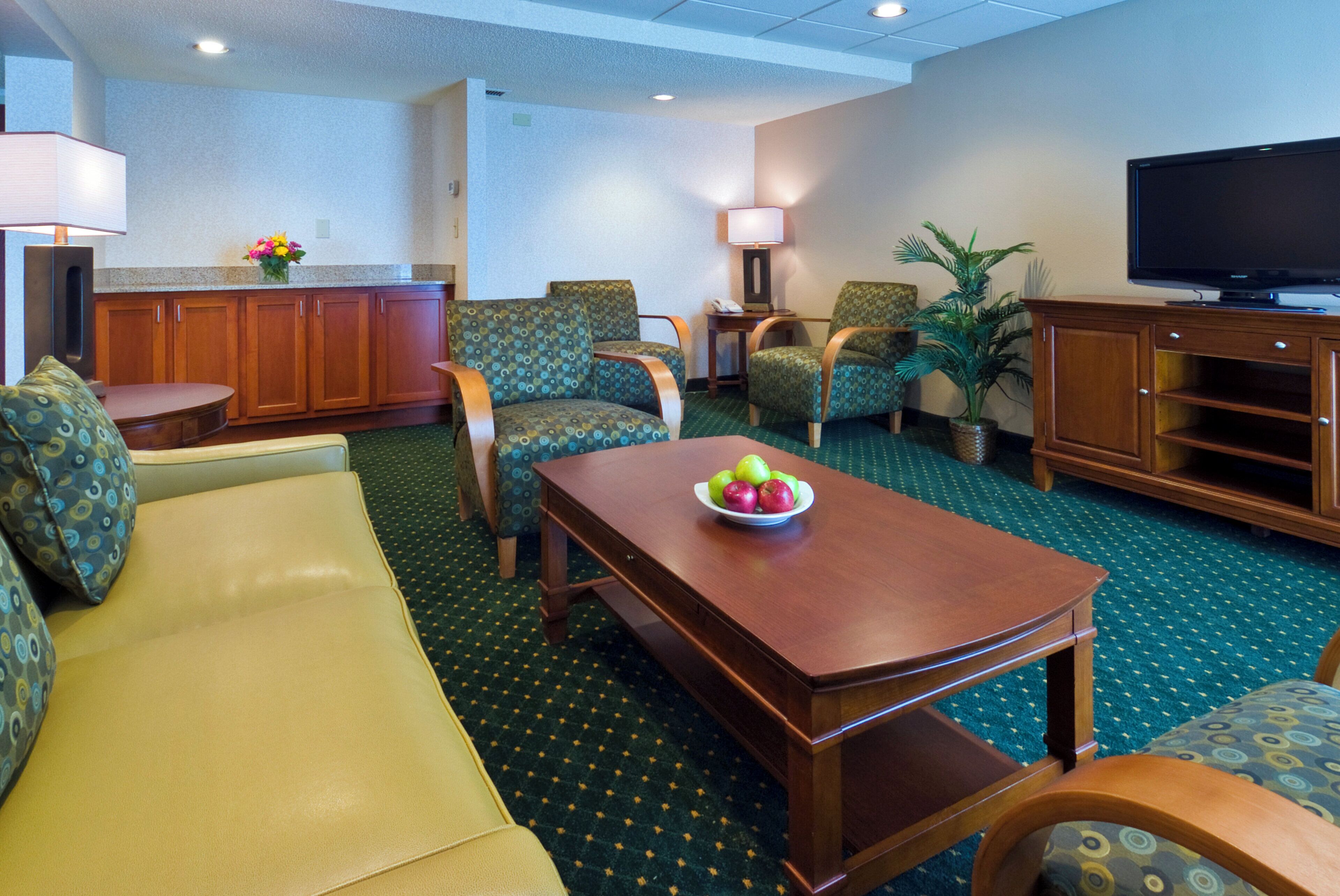 A hotel room with a sofa, chairs, a table with fruit, a television, and a cabinet.