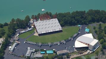 An aerial view of a sports complex with a large stadium, parking areas, and a lake with boats.