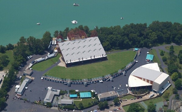 An aerial view of a sports complex with a large stadium, parking areas, and a lake with boats.