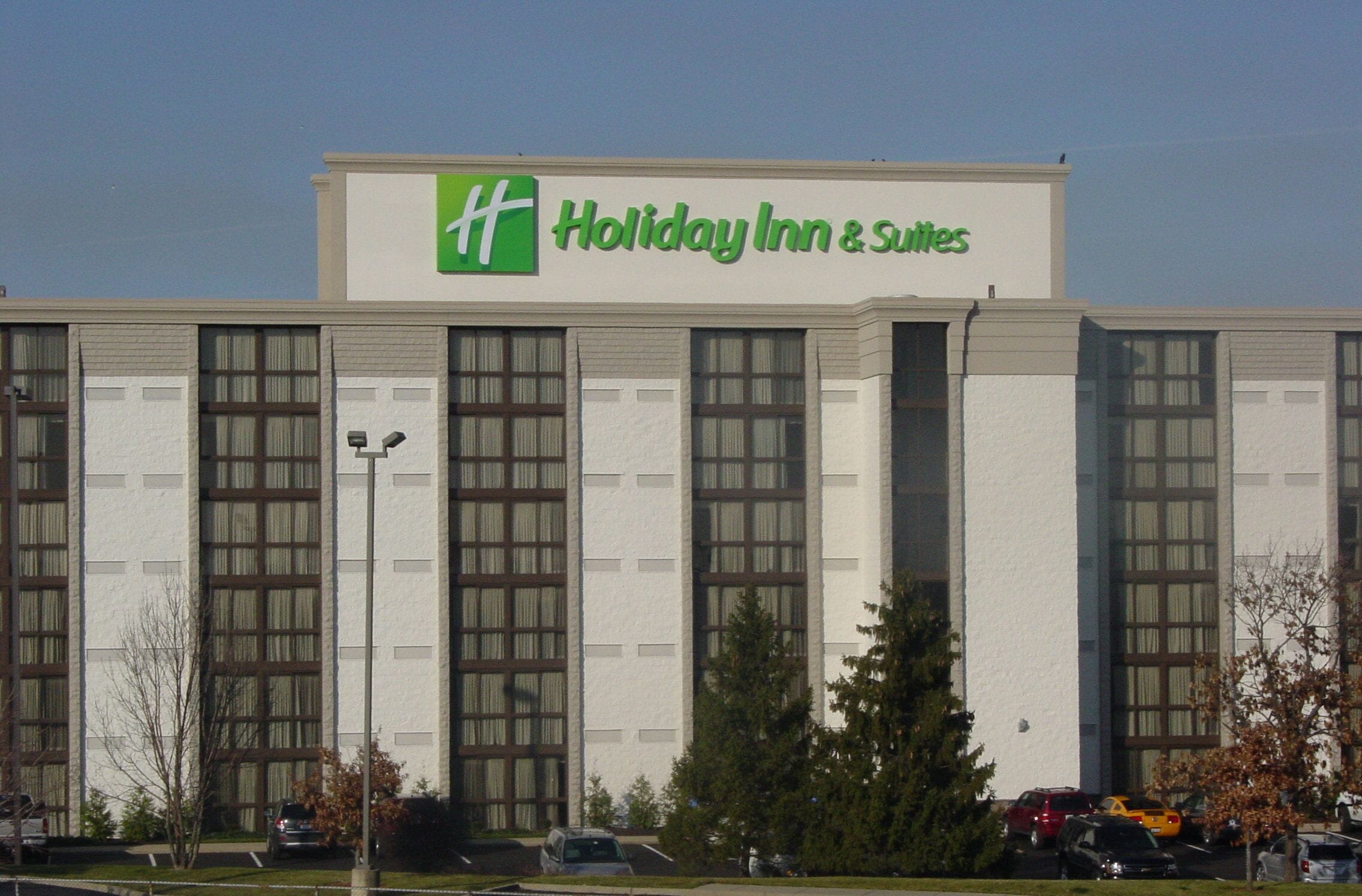 A Holiday Inn & Suites building with a large sign, multiple windows, and a parking lot with cars.