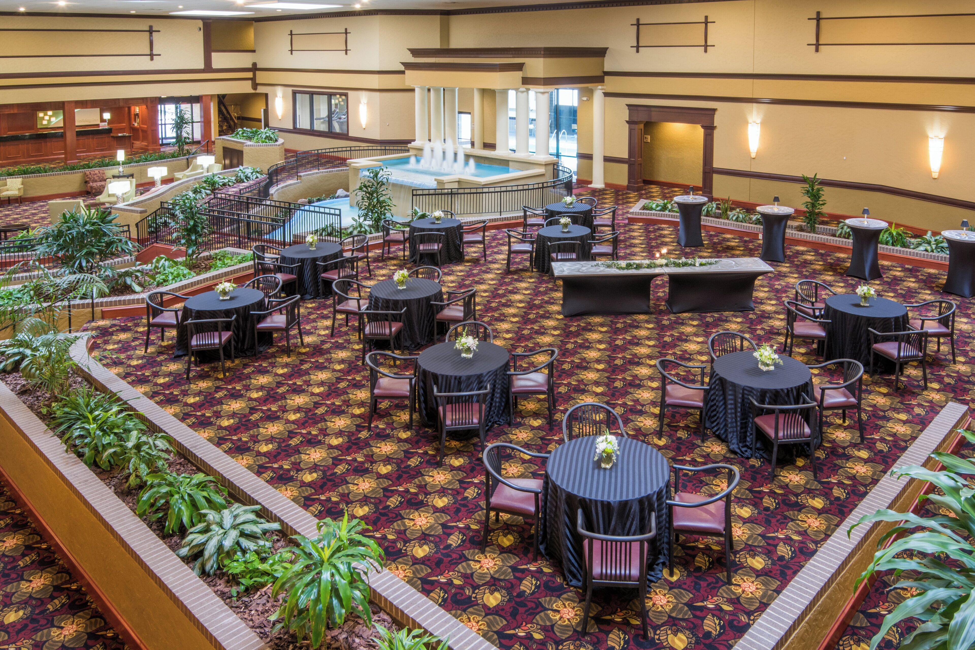A hotel lobby with a central fountain, multiple dining tables with chairs, and a patterned carpet.