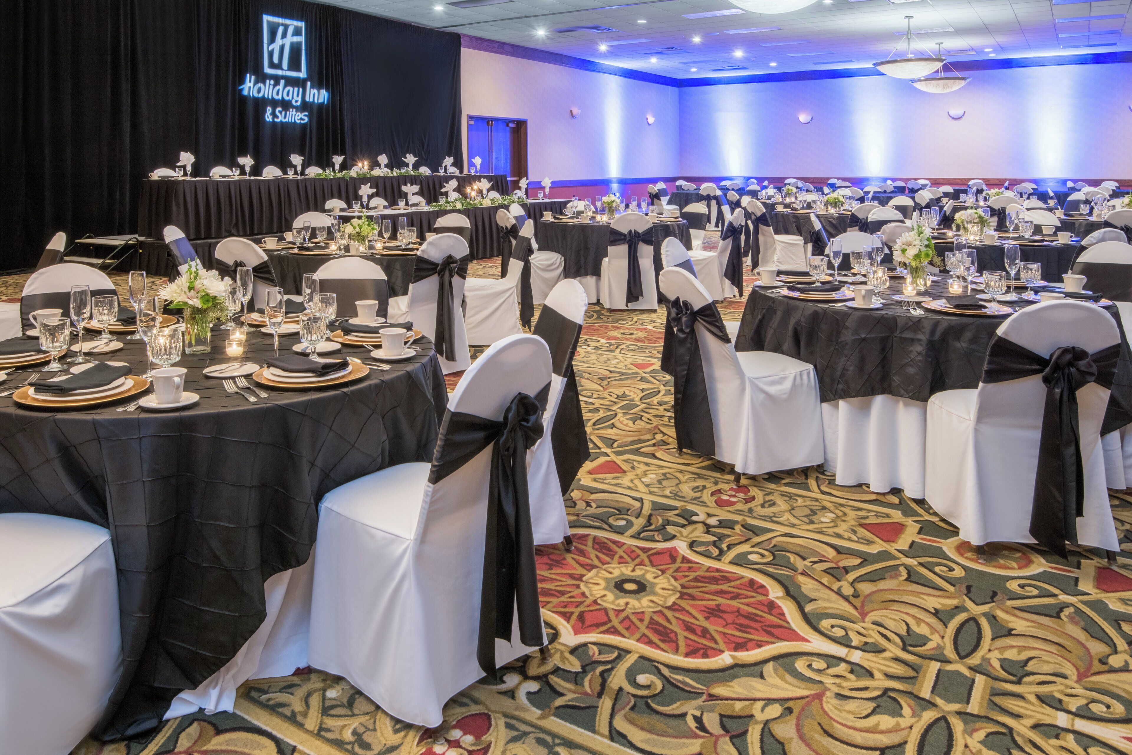 A banquet hall with round tables, white chairs, and black tablecloths.