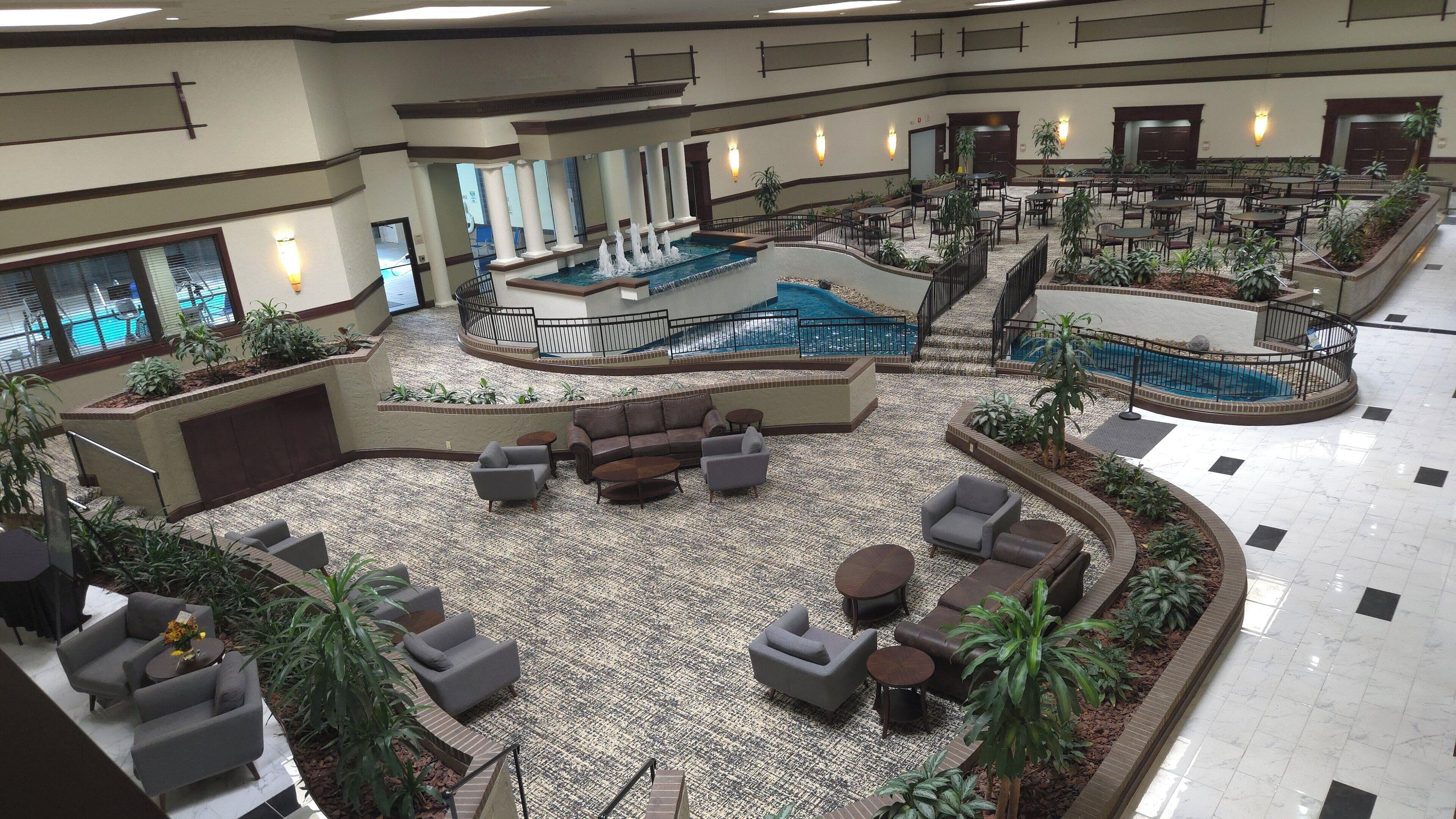 A spacious indoor area with a central pool, multiple seating areas, and a variety of plants.