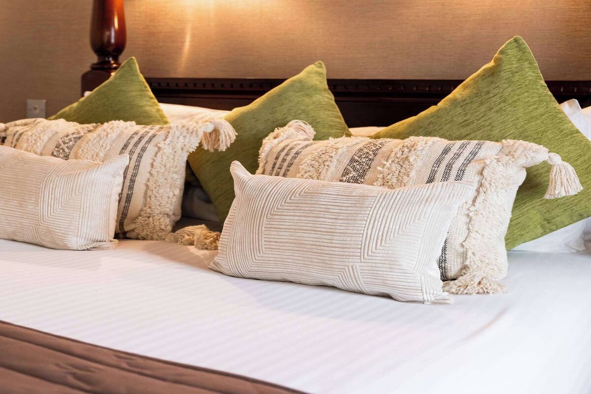 A neatly made bed with multiple pillows and a green throw blanket.