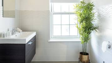 Un baño moderno con tocador blanco, inodoro y ventana con persianas.