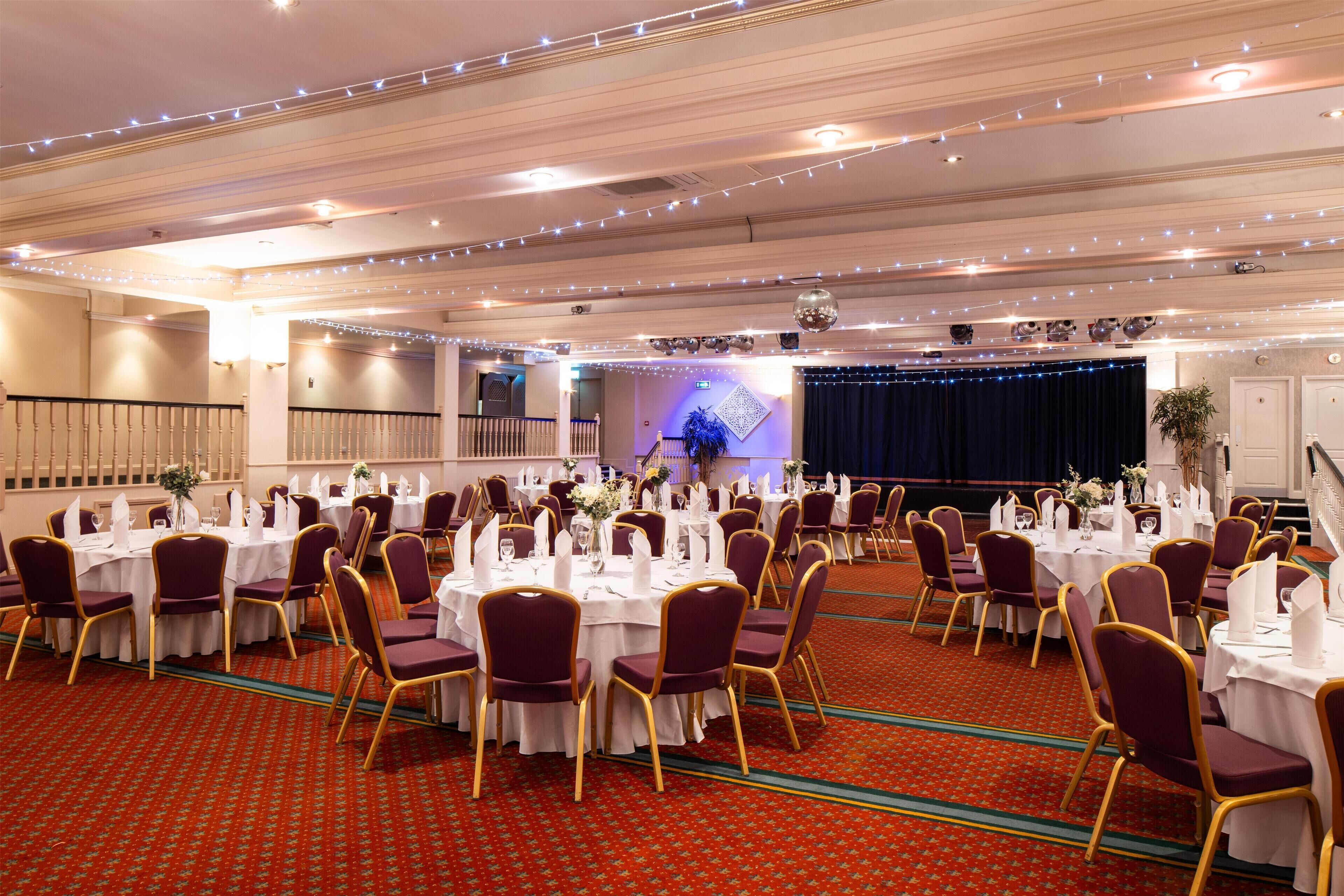 Un salón de banquetes con mesas redondas, sillas y un escenario.