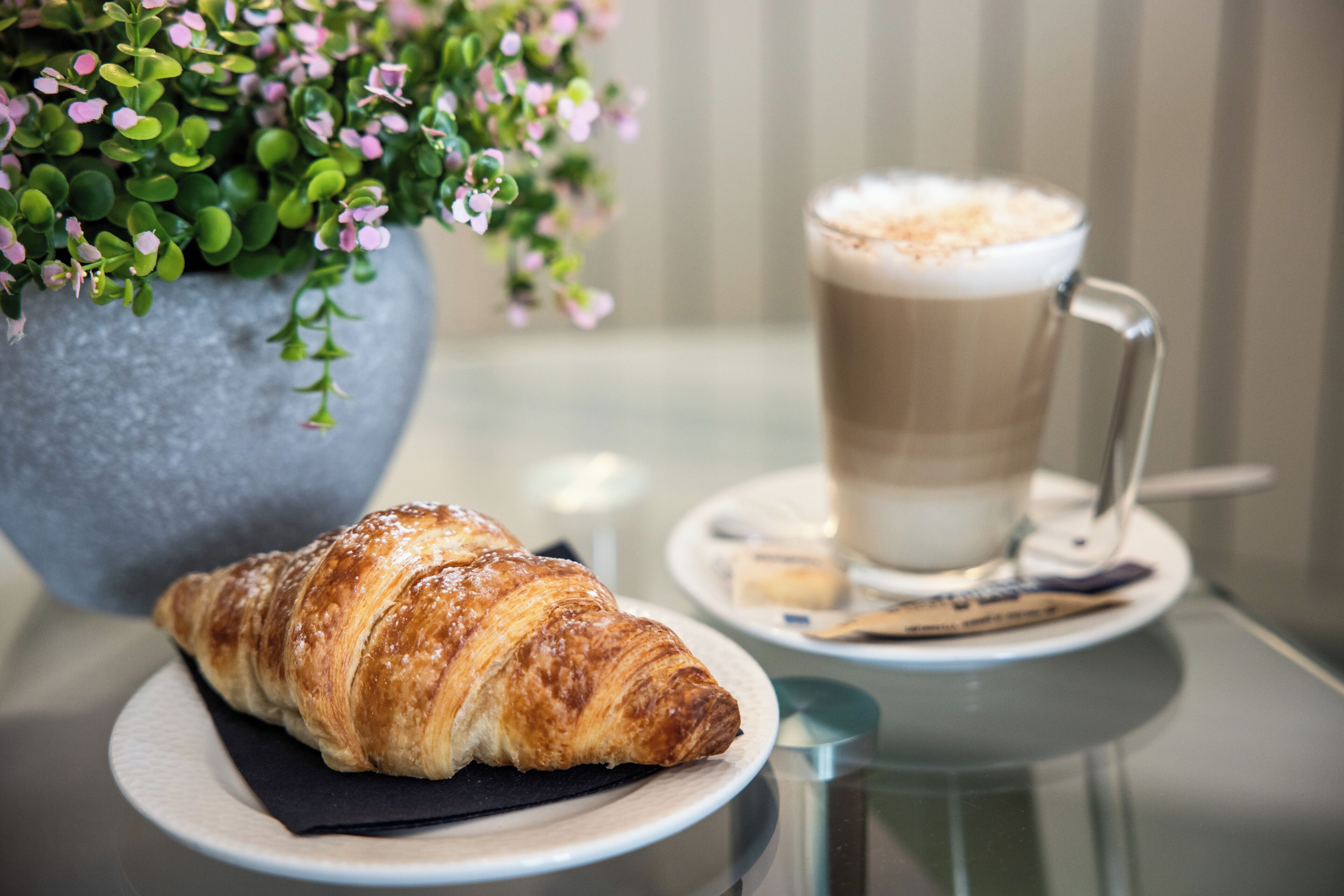 Un croissant sur une assiette, une tasse de café et une plante en pot.