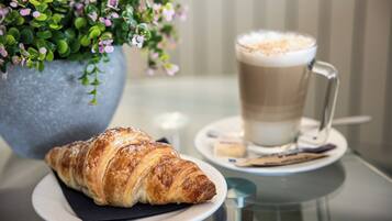 Un croissant sur une assiette, une tasse de café et une plante en pot.